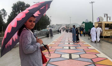A woman walks with an umbrella along a promontory in Al-Namas in Saudi Arabia's Asir province, on August 16, 2022. (AFP)